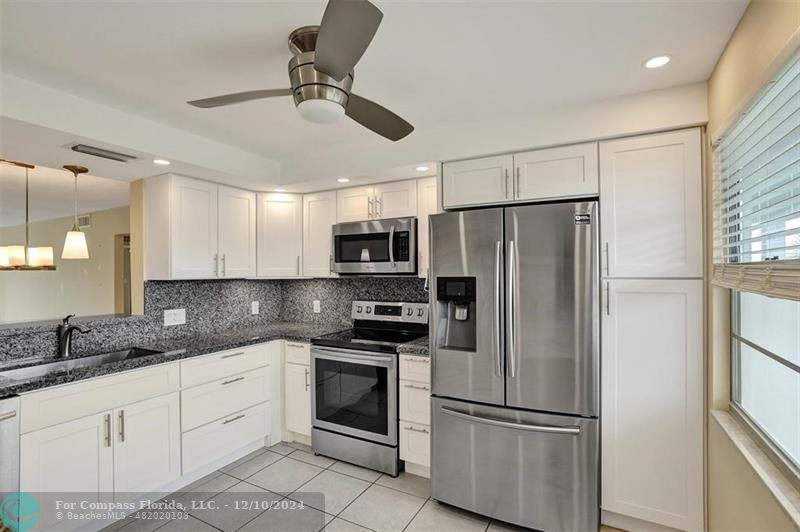 a kitchen with stainless steel appliances granite countertop a refrigerator a stove a sink and white cabinets