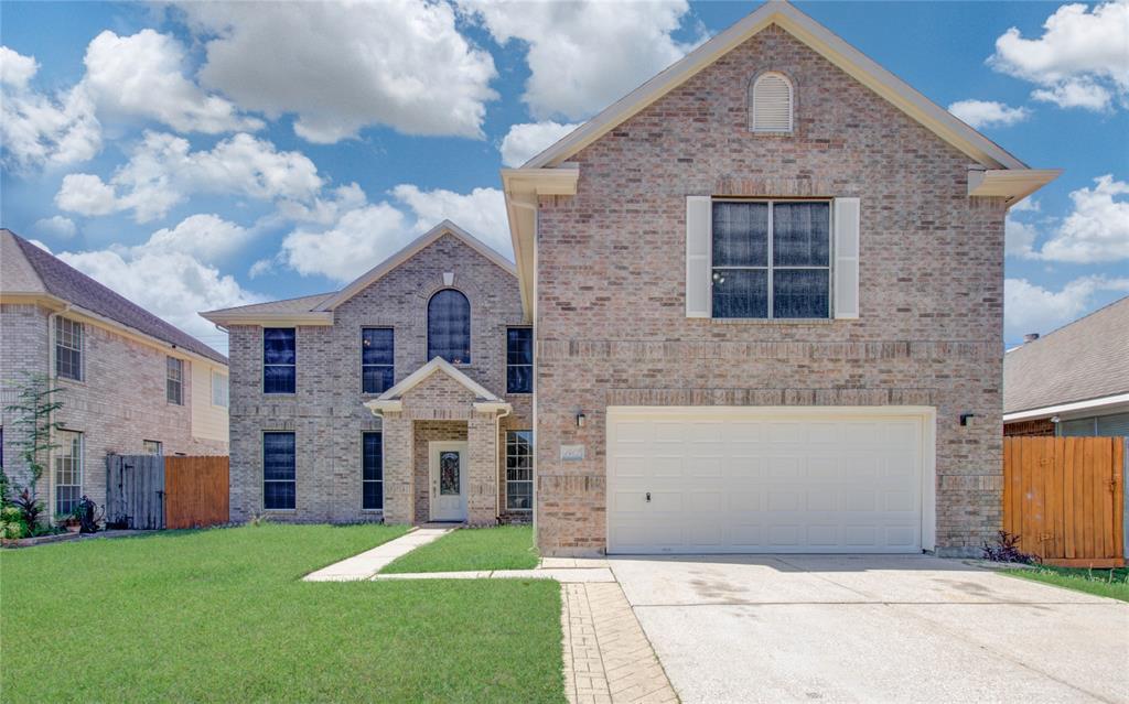 This is a two-story brick home featuring a prominent entryway with an arched transom window, a two-car garage, and large windows that allow for ample natural light. The property includes a well-maintained lawn and is situated in a suburban neighborhood with adjacent homes.