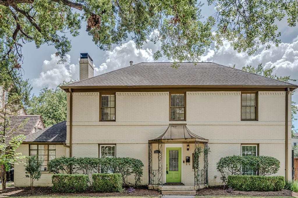 Two-story traditional brick home featuring a symmetrical facade with a central entryway, flanked by multi-pane windows and framed by manicured shrubbery. The property includes a well-kept lawn and a pathway leading to the vibrant front door.