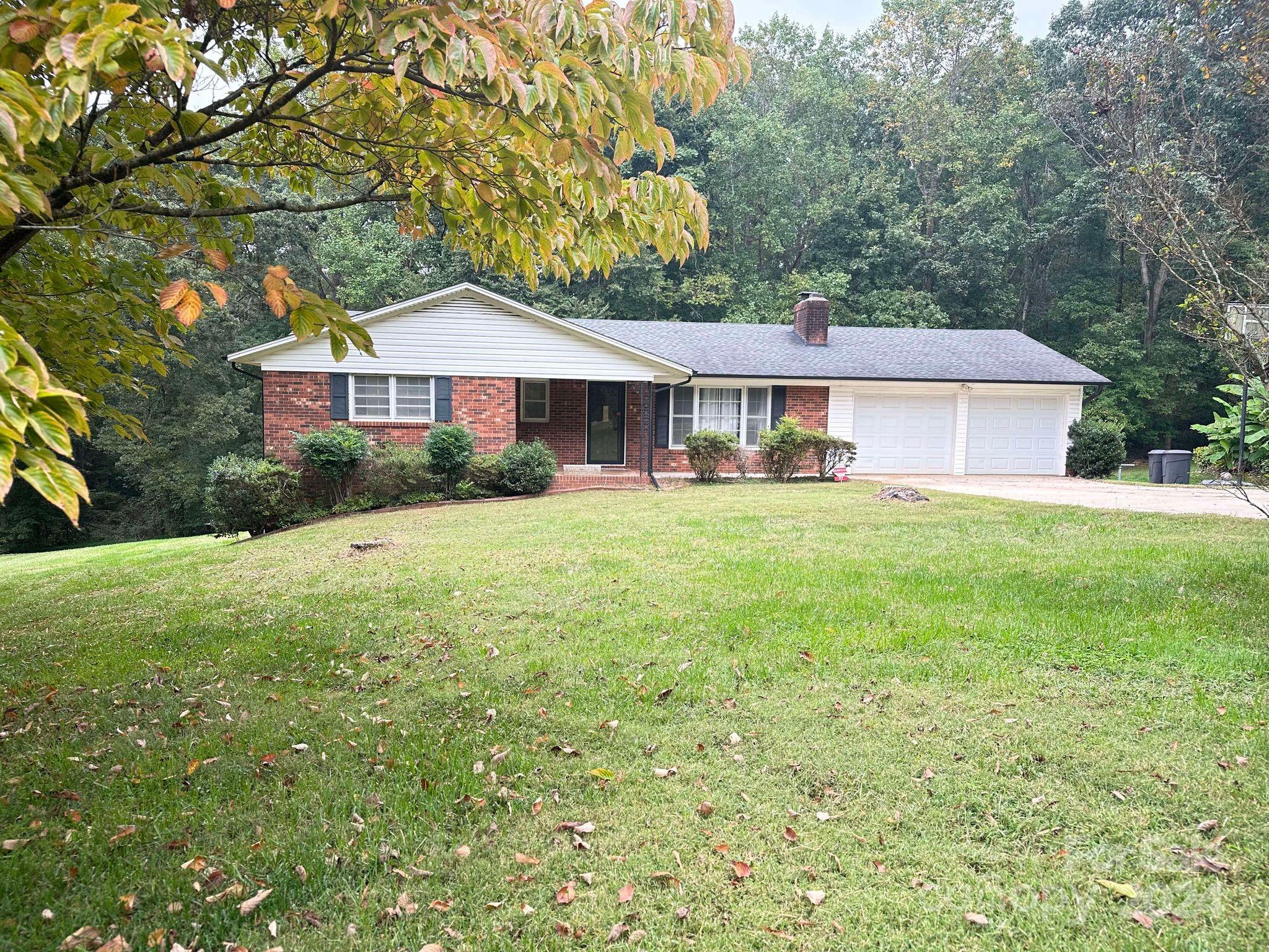 a house that is sitting in the grass with large trees and plants