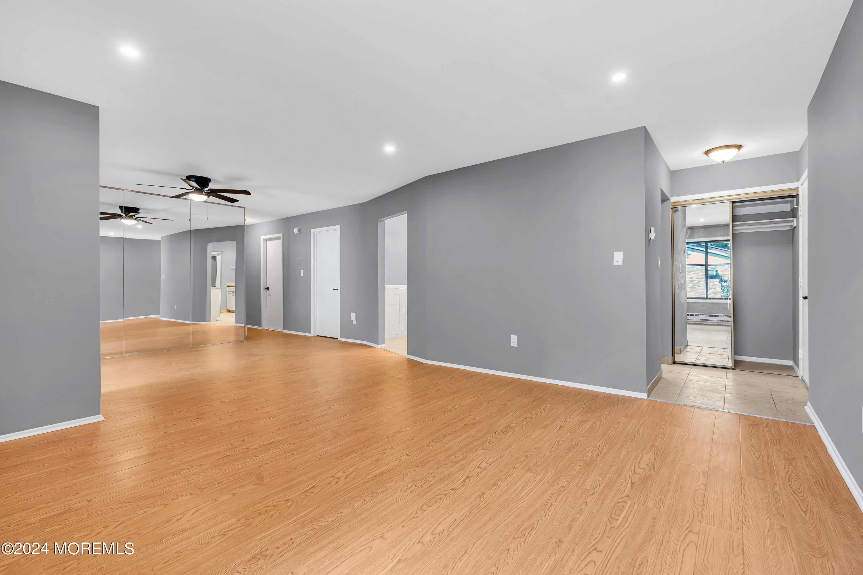 a view of an empty room with wooden floor and a ceiling fan