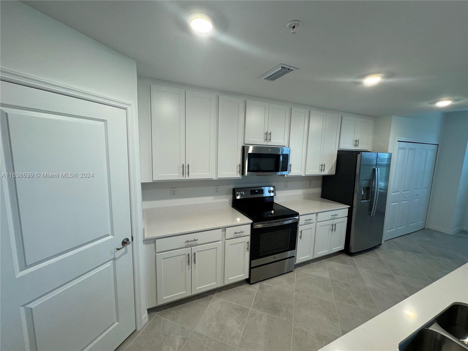 a kitchen with stainless steel appliances a refrigerator a sink and white cabinets