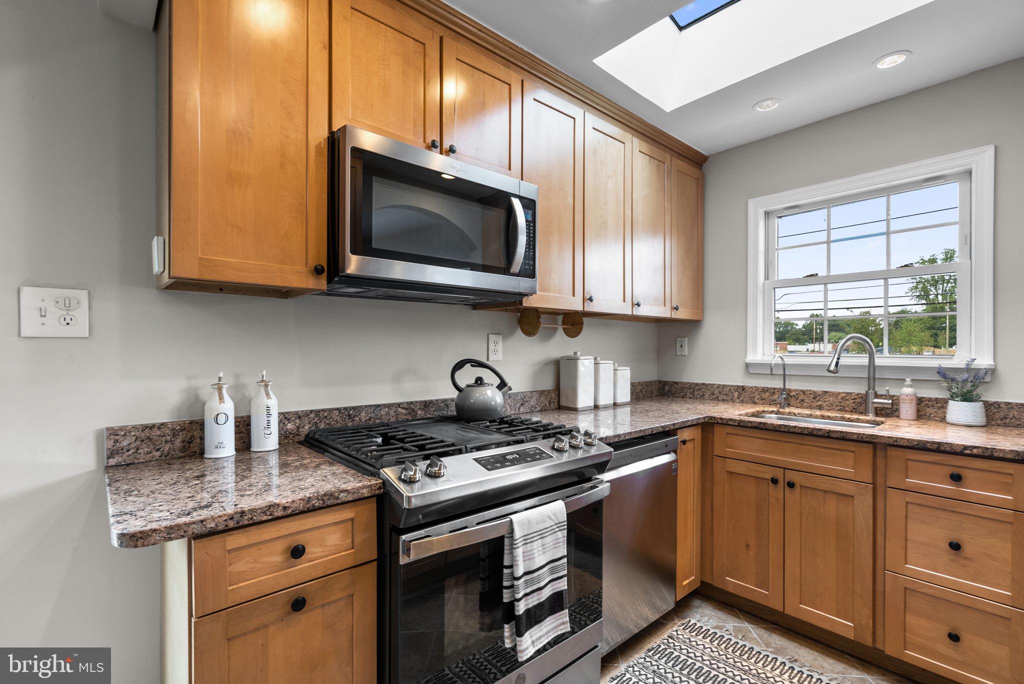 a kitchen with stainless steel appliances granite countertop a sink a stove a microwave and wooden cabinets