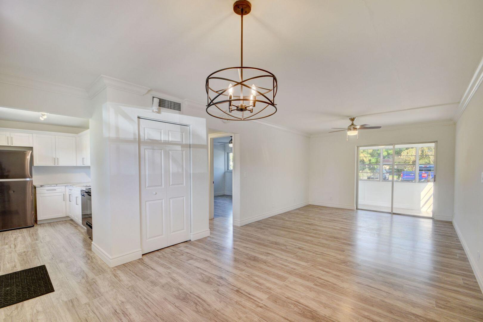 a view of an empty room and kitchen with wooden floor and window