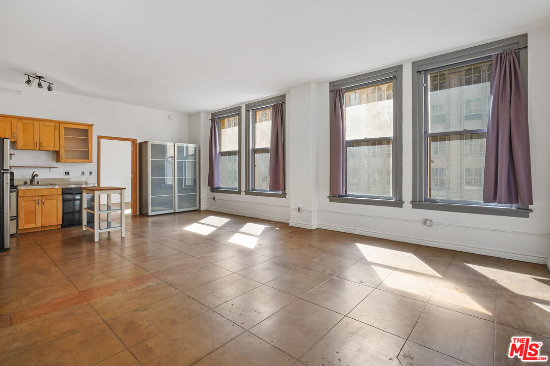 a view of an empty room with window and kitchen view