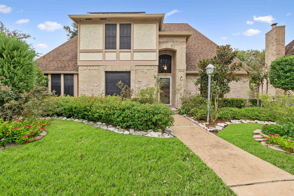 Charming two-story home with a brick exterior, lush landscaping, and a welcoming walkway leading to the entrance. 