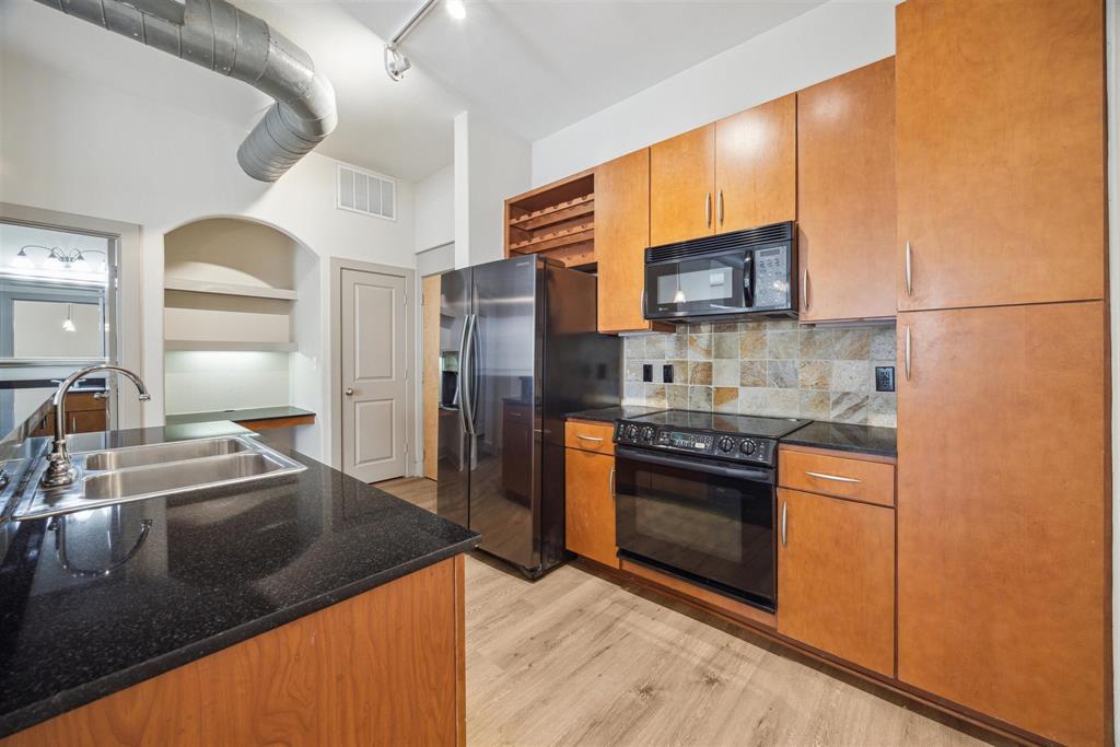 a kitchen with stainless steel appliances granite countertop a refrigerator a stove and a sink with wooden floors