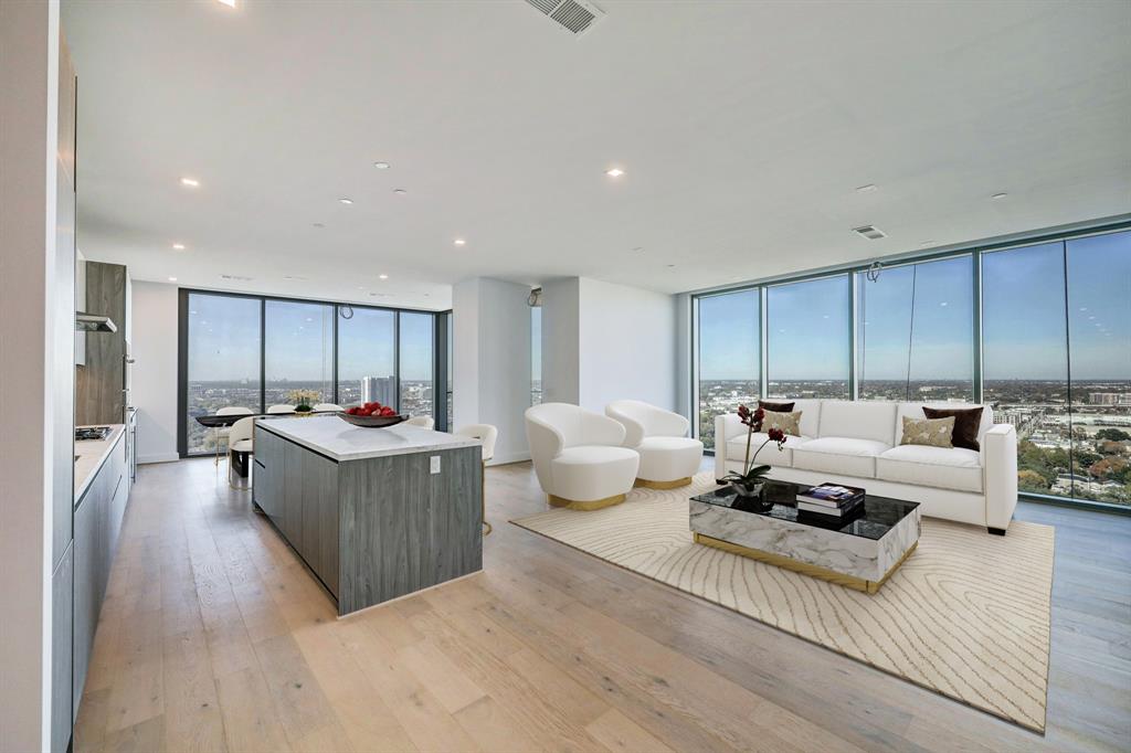 The Residences at The Allen, Houston’s premiere Luxury Condo Hotel Tower on Allen Parkway, Houston, stands gracefully against the skyline. Its modern design and glass windows exude sophistication, while a warm glow from the setting sun highlights its elegance. Living room virtually staged.