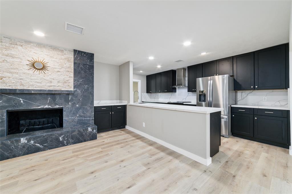 A stunning wood-burning fireplace with an elegant tile surround balances the kitchen's contrasting black and white color tones.