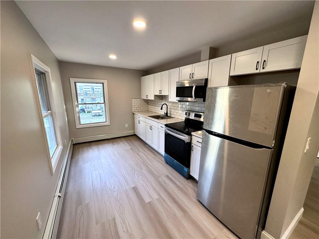 Kitchen featuring white cabinets, sink, backsplash, light wood-type flooring, and appliances with stainless steel finishes