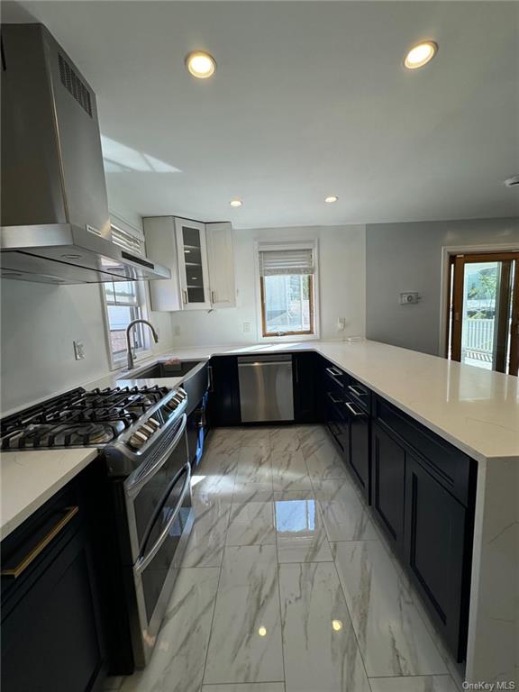 Kitchen featuring white cabinetry, stainless steel appliances, wall chimney range hood, and a wealth of natural light