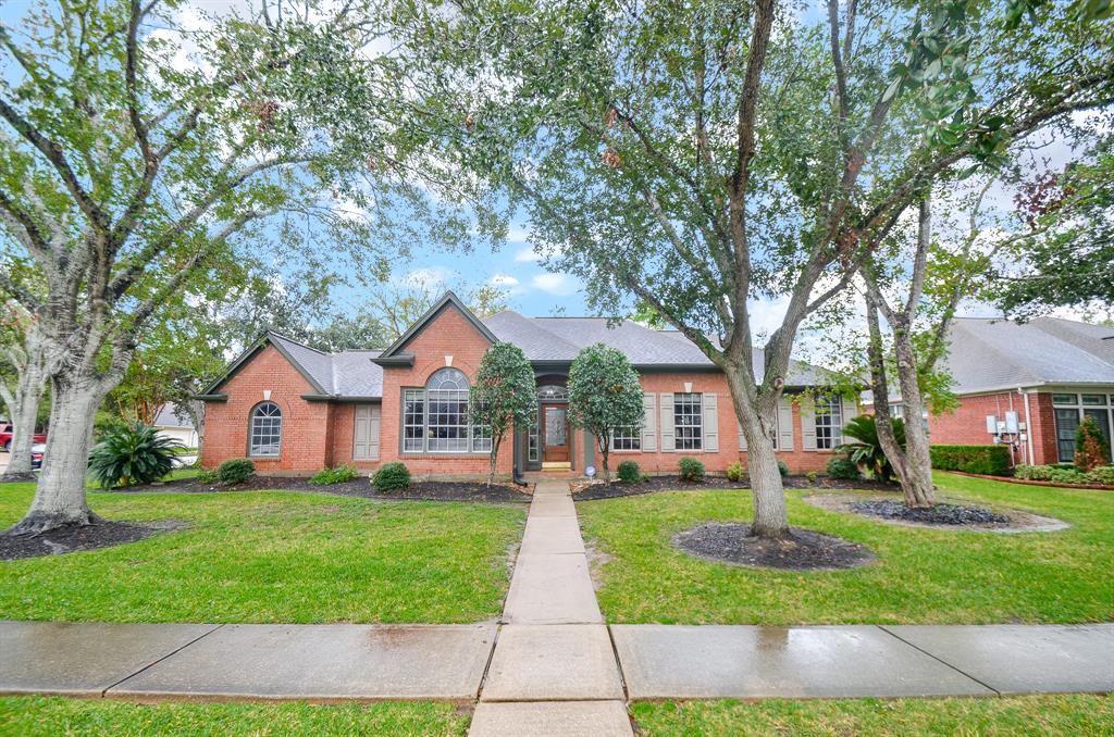 Charming single-story brick home with mature trees, and an inviting walkway leading to a central entrance. The property features a traditional design, nestled in a serene neighborhood setting.