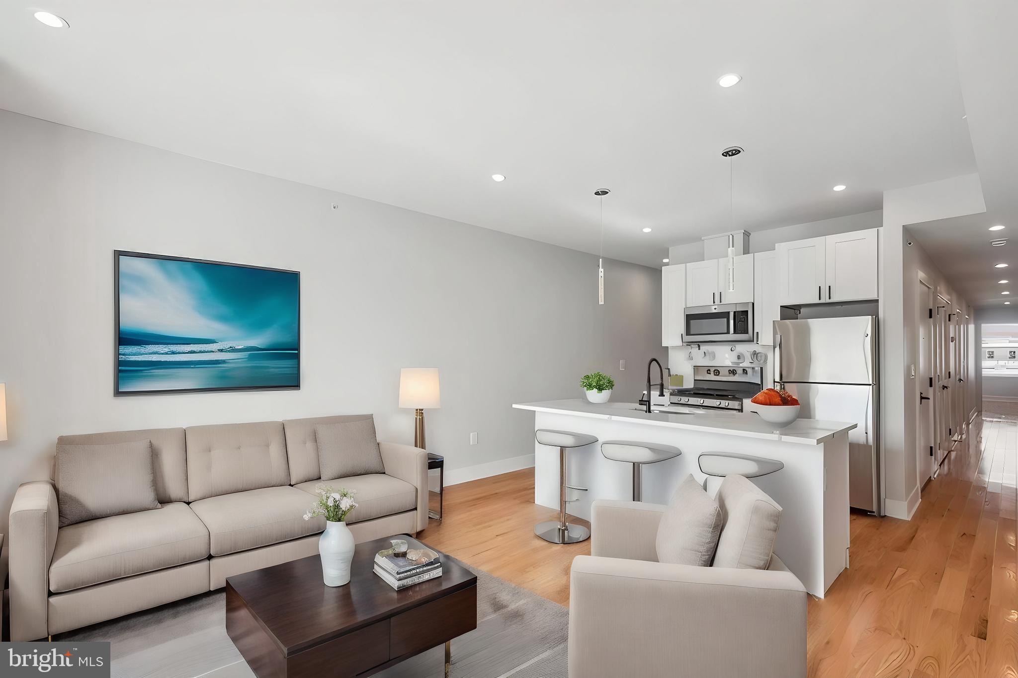 a living room with stainless steel appliances furniture a rug and a kitchen view