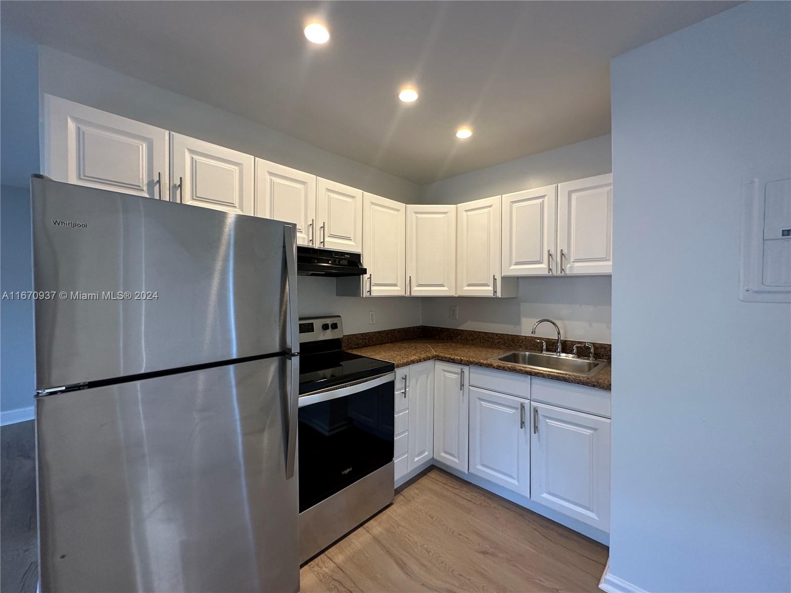 a kitchen with stainless steel appliances granite countertop a refrigerator a sink and white cabinets