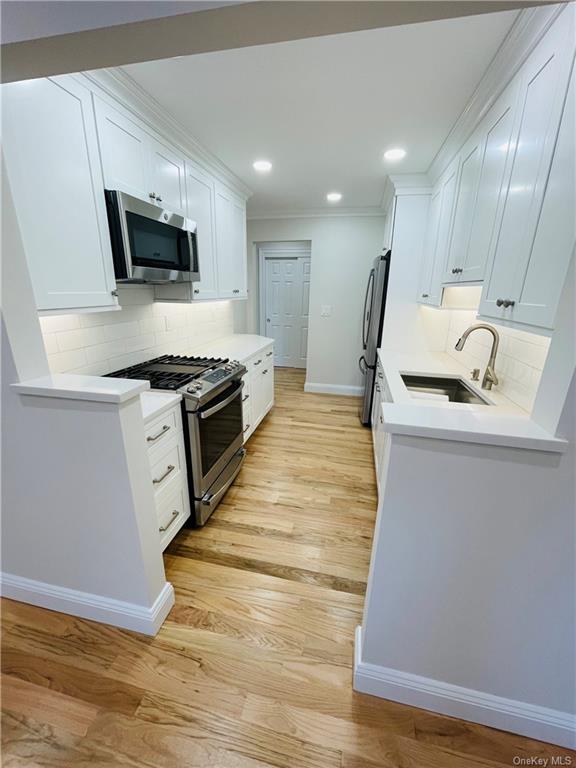 Kitchen featuring decorative backsplash, white cabinetry, stainless steel appliances, light wood-type flooring, and sink