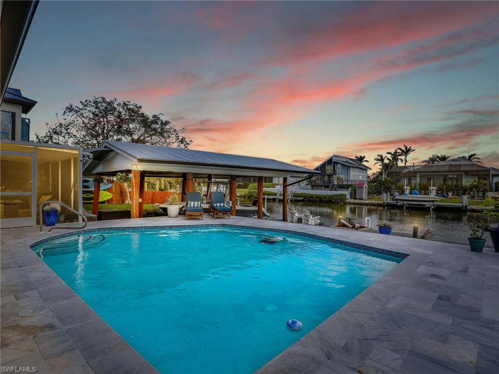 Pool at dusk featuring a patio, a dock, a gazebo, and a water view