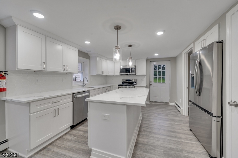 a kitchen with stainless steel appliances kitchen island granite countertop a refrigerator a sink dishwasher a stove and white cabinets with wooden floor