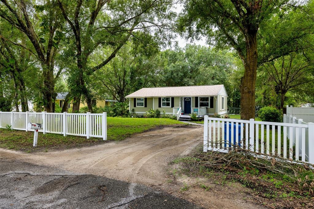 a view of a white house with a small yard and large trees