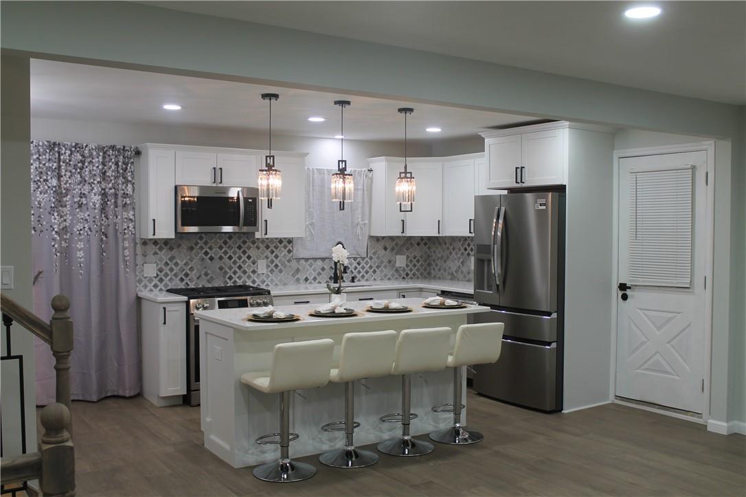 Kitchen with a kitchen island, appliances with stainless steel finishes, hanging light fixtures, dark wood-type flooring, and white cabinets