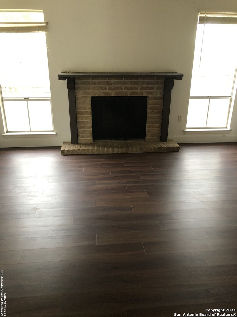 an empty room with wooden floor fireplace and windows