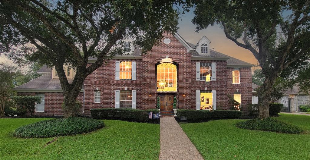 This is a two-story brick house with large windows, a prominent front entry, and mature trees in the front yard, offering both curb appeal and shade.