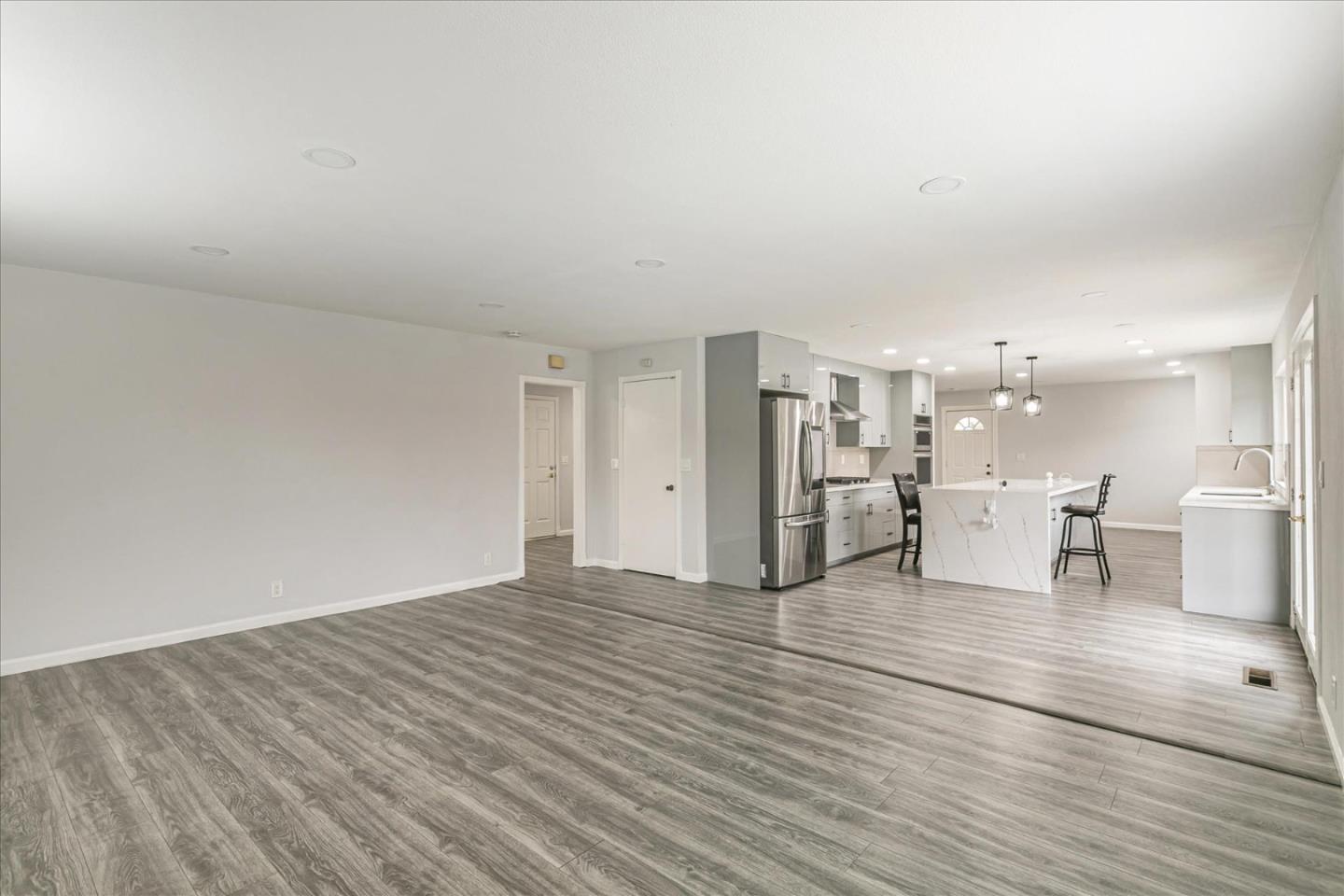 a view of an empty room and kitchen with wooden floor