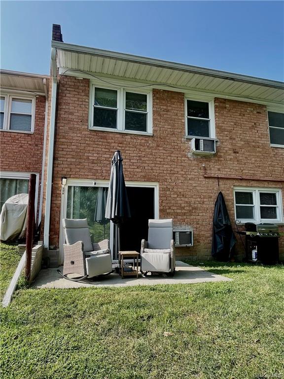 Rear view of house with a lawn, a patio area, and a wall mounted air conditioner