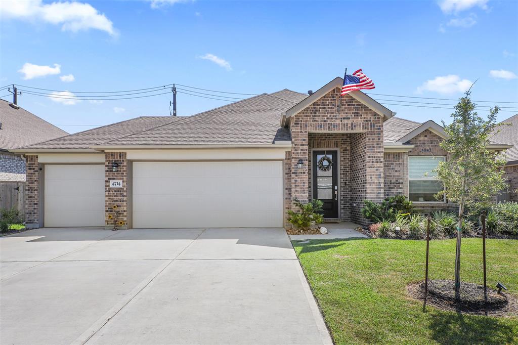 This is a single-story brick home featuring a three-car garage, a well-maintained front lawn, and a welcoming entrance with an American flag on display.