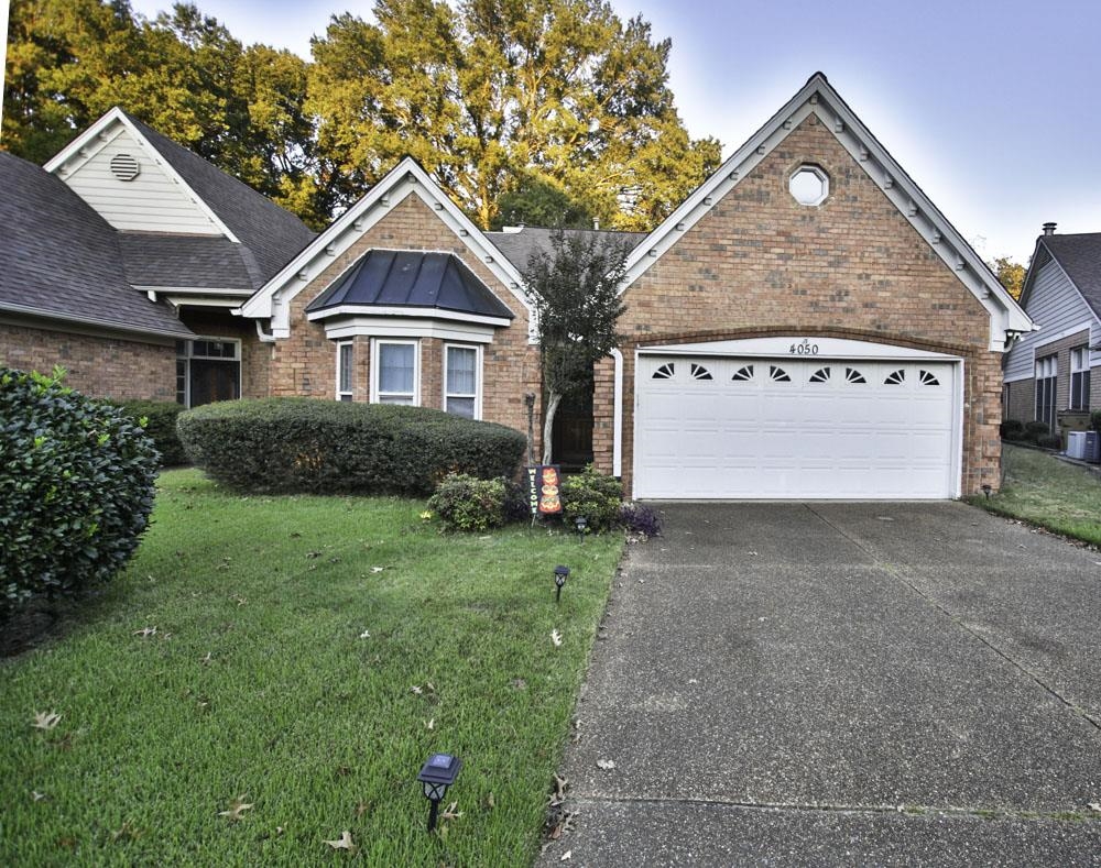 View of front of property featuring a front yard, a garage, and cooling unit