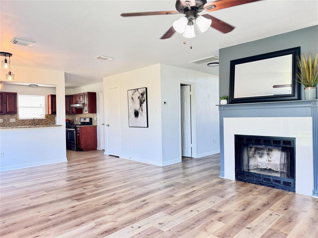 a view of a livingroom with a fireplace a ceiling fan and kitchen view