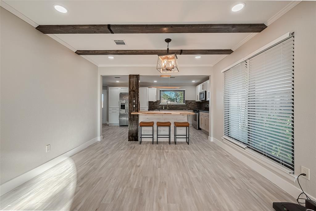 This is a modern, open-concept living space featuring a combined kitchen and dining area with stylish wood beam accents, a chic pendant light fixture, large windows for ample natural light, and sleek wood-look flooring.