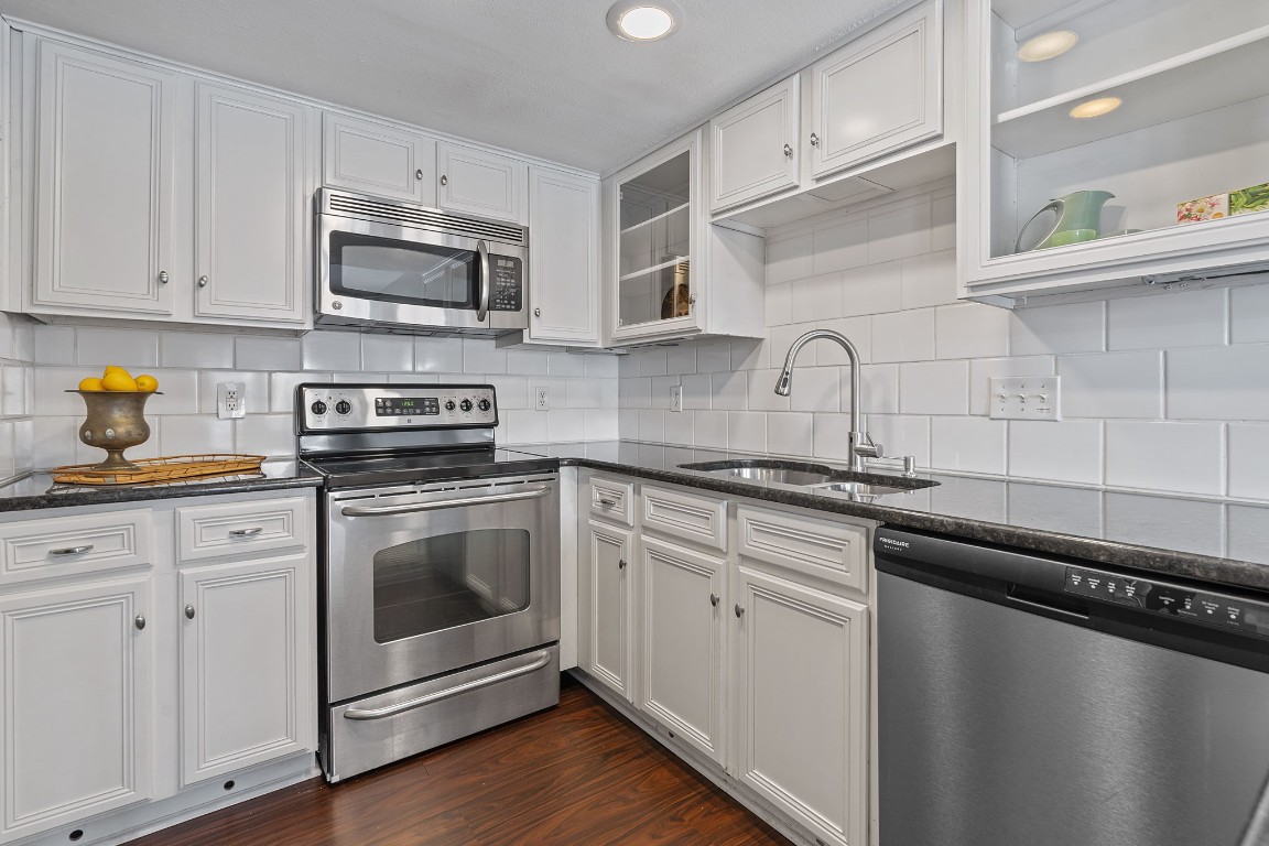 a kitchen with stainless steel appliances granite countertop white cabinets a sink a stove a microwave and wooden floors