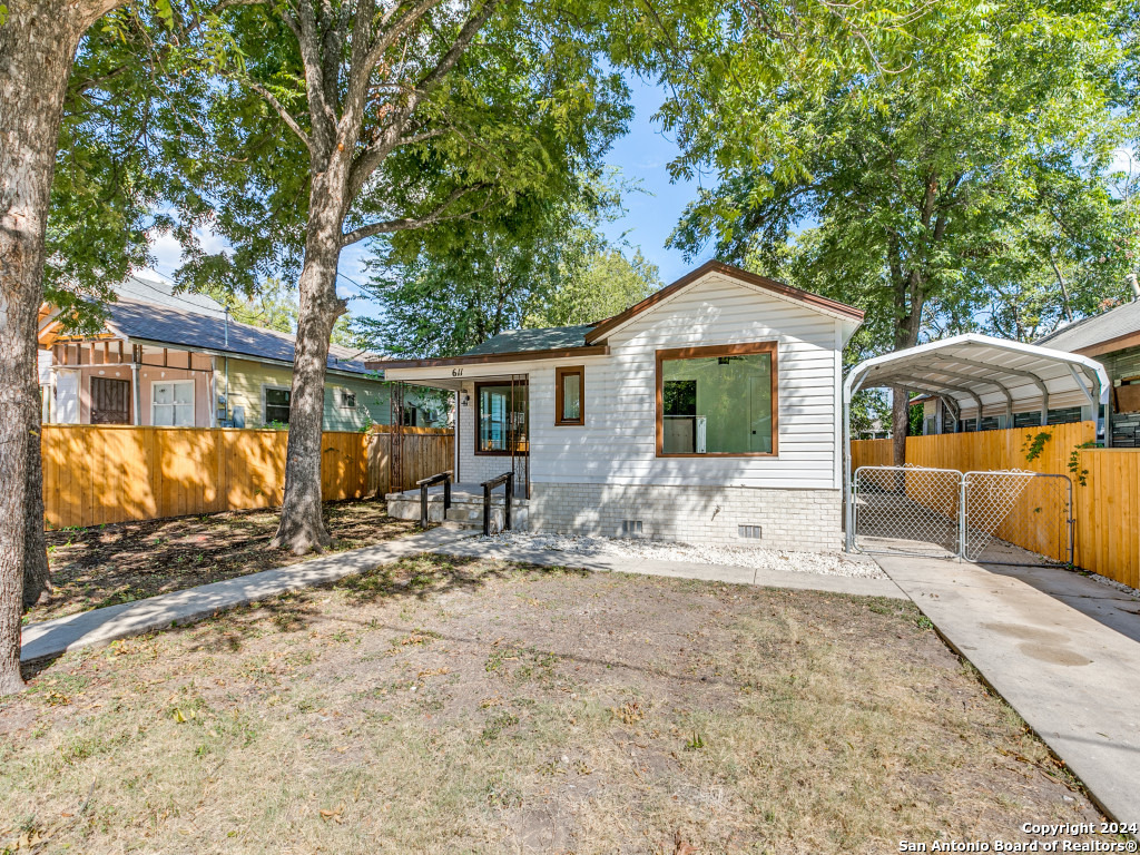 a front view of a house with large trees and wooden fence