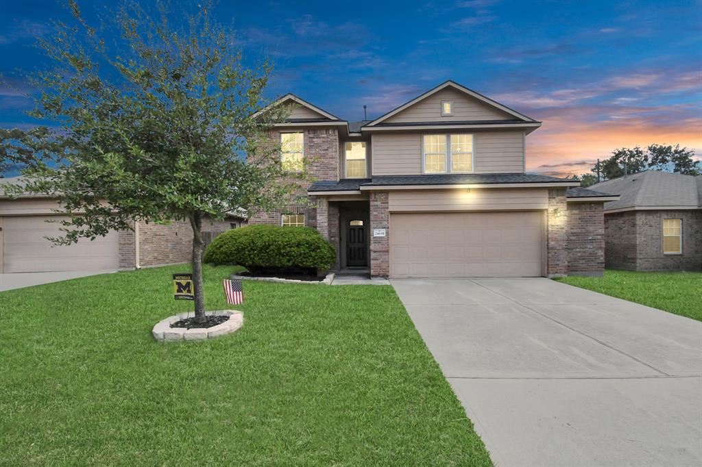 This lovely two-story suburban home with a brick facade, featuring a two-car garage and a well-maintained lawn. A single tree decorates the front yard.