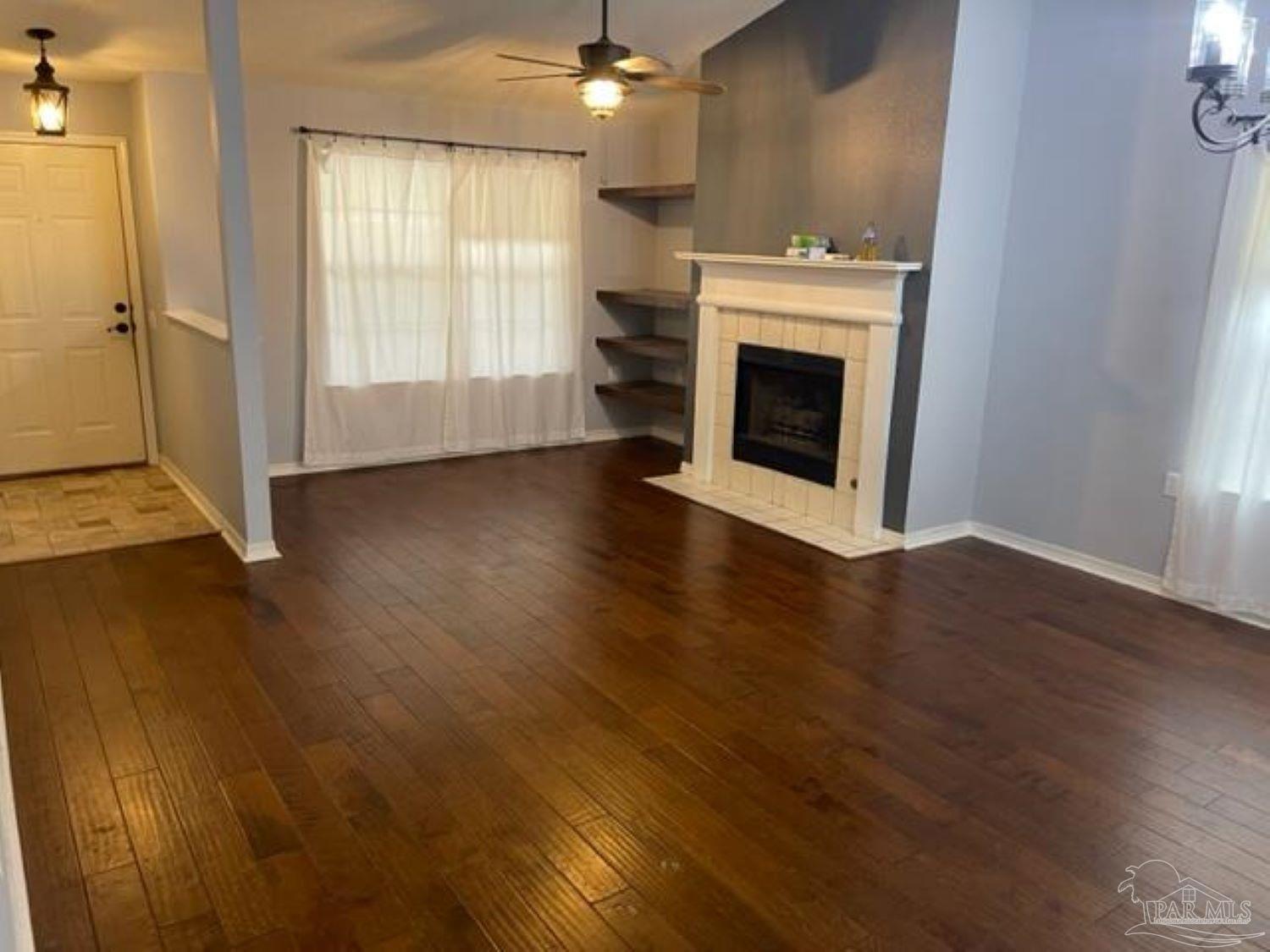 an empty room with wooden floor fireplace and windows