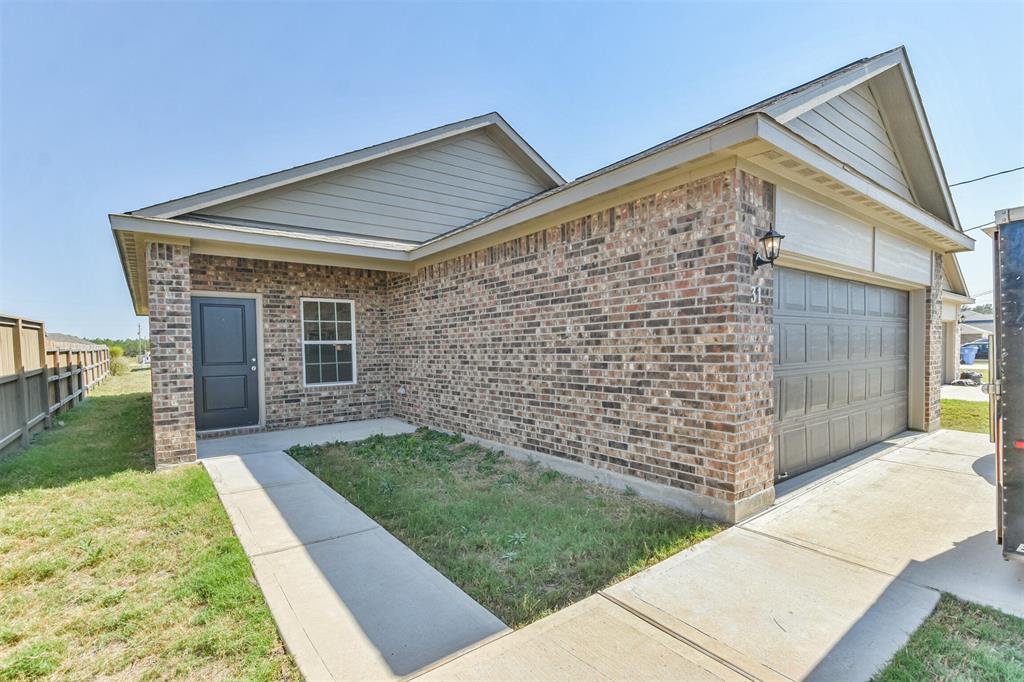 This is a single-story brick home featuring a two-car garage, a covered entryway, and a side fence, with a clear sky in the background.