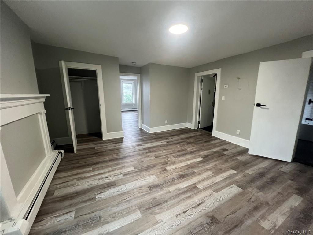 Unfurnished bedroom with a closet, wood-type flooring, baseboard heating, and a spacious closet