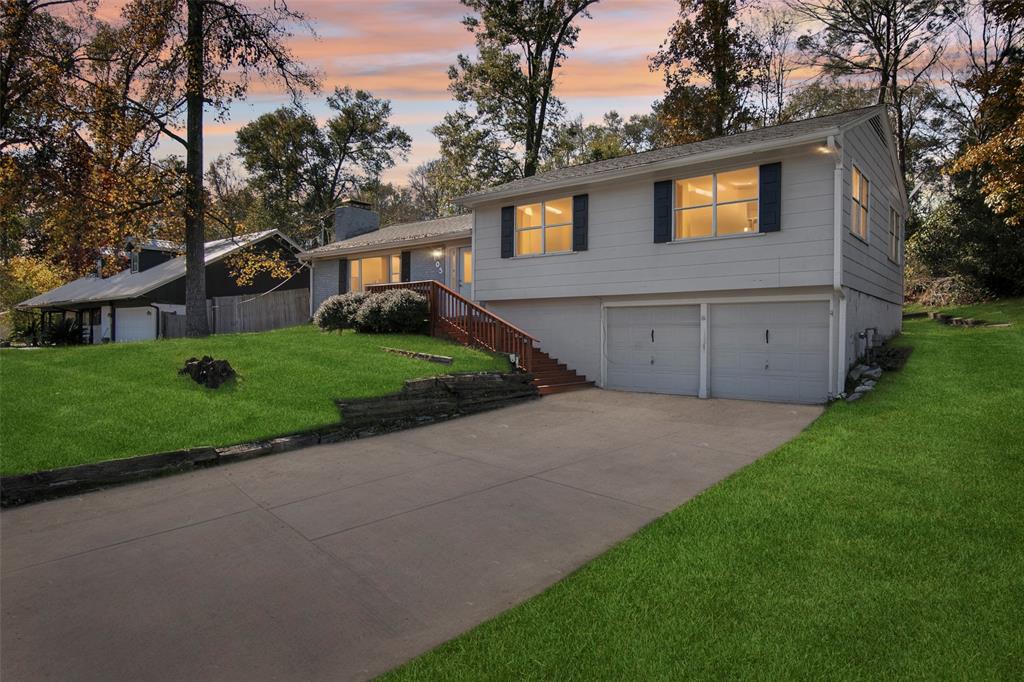 This inviting home features a spacious front yard with well-maintained landscaping. It has a two-car garage, large windows, and a classic design, situated in a peaceful, wooded setting.