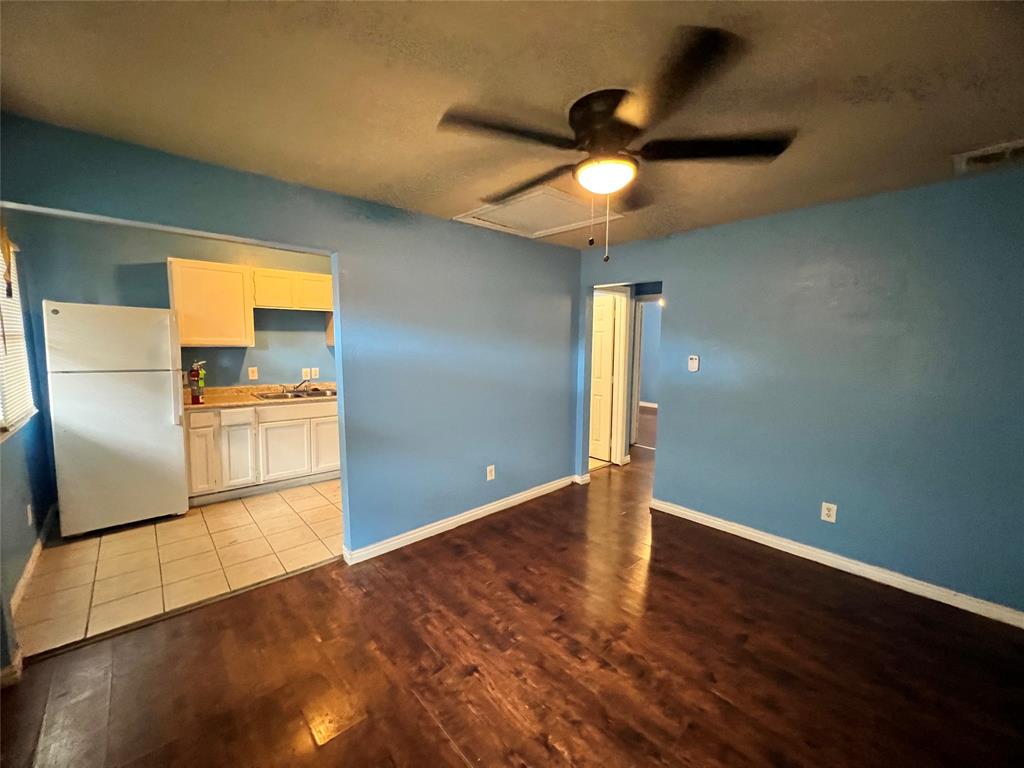 an empty room with wooden floor a ceiling fan and kitchen view