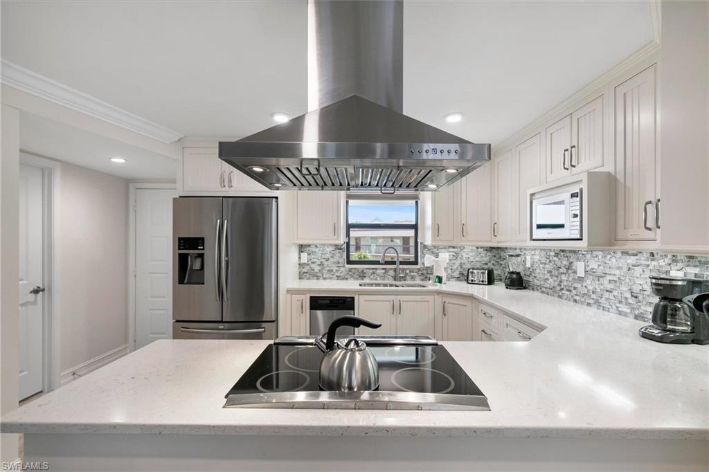 Kitchen with white cabinets, stainless steel appliances, island exhaust hood, tasteful backsplash, and sink