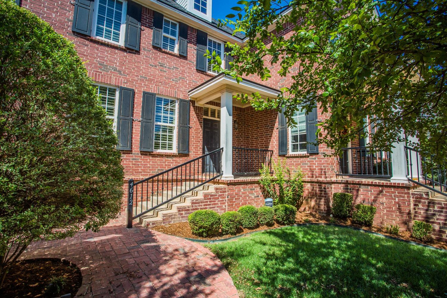 a view of a brick house with a yard plants and large tree