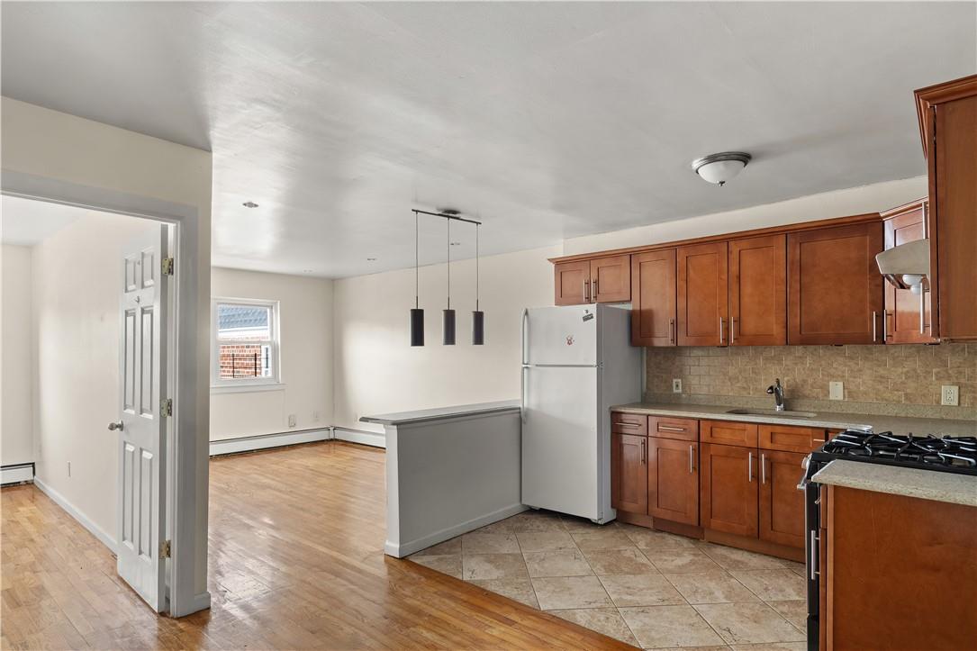 Kitchen featuring white refrigerator, tasteful backsplash, decorative light fixtures, stainless steel gas range, and light wood-type flooring