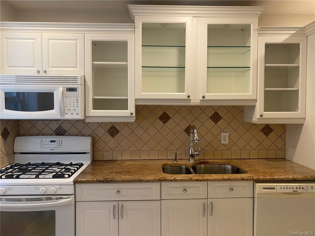 Kitchen featuring backsplash, sink, white cabinetry, and white appliances