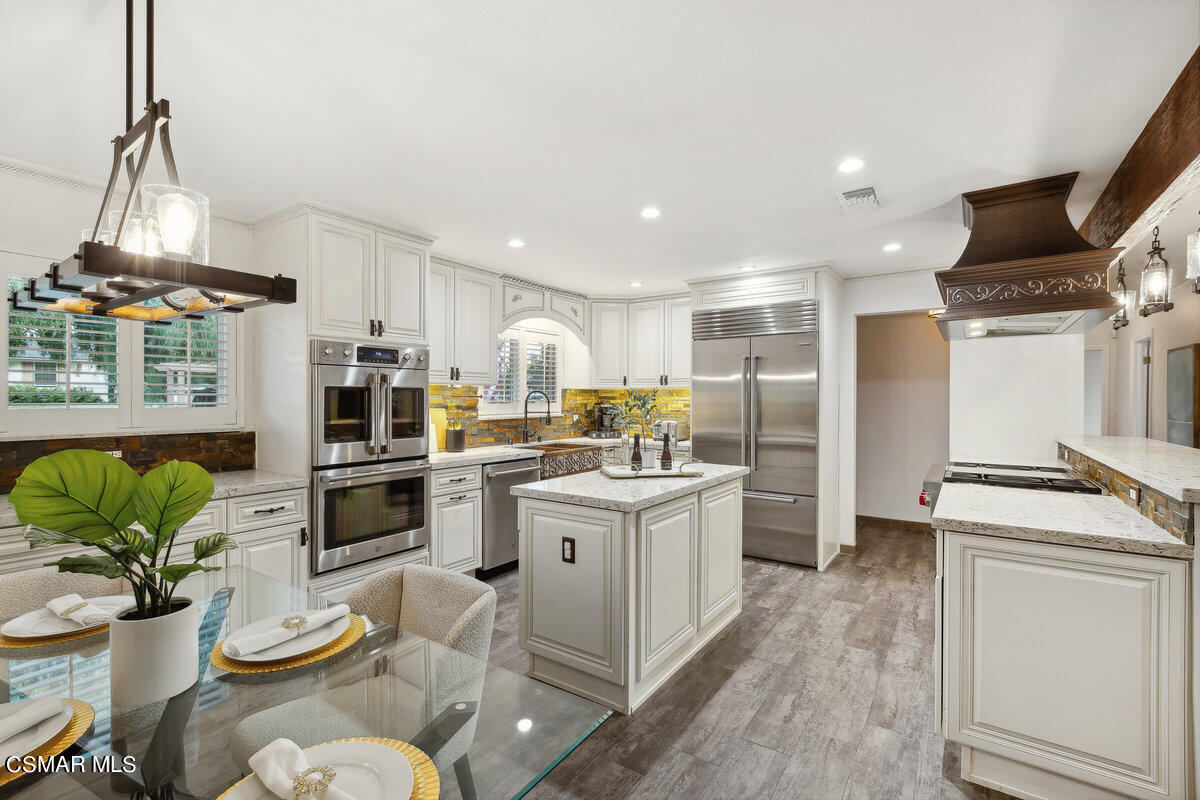 a kitchen with stainless steel appliances kitchen island granite countertop a refrigerator a stove a sink dishwasher and white cabinets with wooden floor