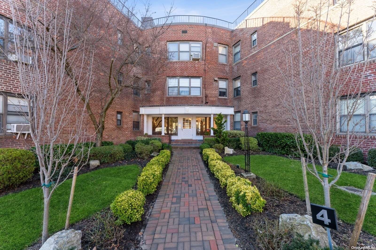 a view of a brick building next to a big yard and large trees