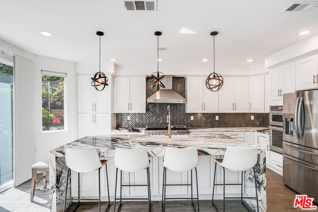 a kitchen with stainless steel appliances kitchen island granite countertop a dining table chairs and white cabinets