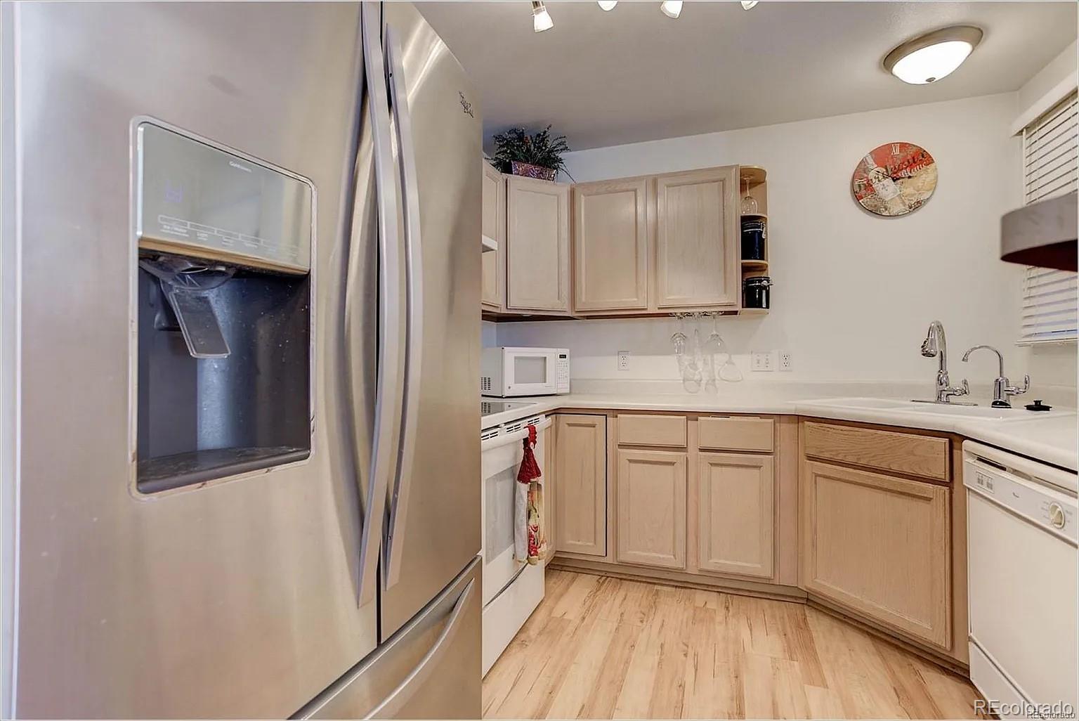 a kitchen with stainless steel appliances granite countertop a refrigerator a sink and white cabinets with wooden floor