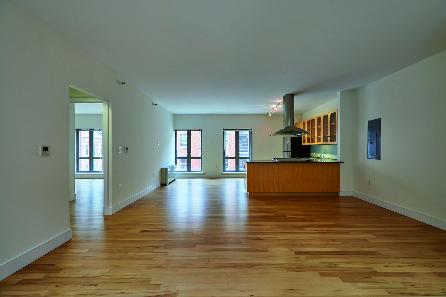 a view of empty room with wooden floor and kitchen