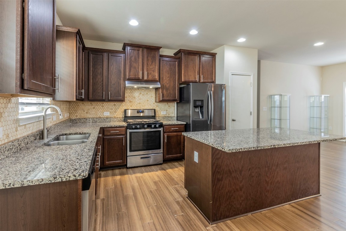 a kitchen with kitchen island granite countertop a sink cabinets and stainless steel appliances