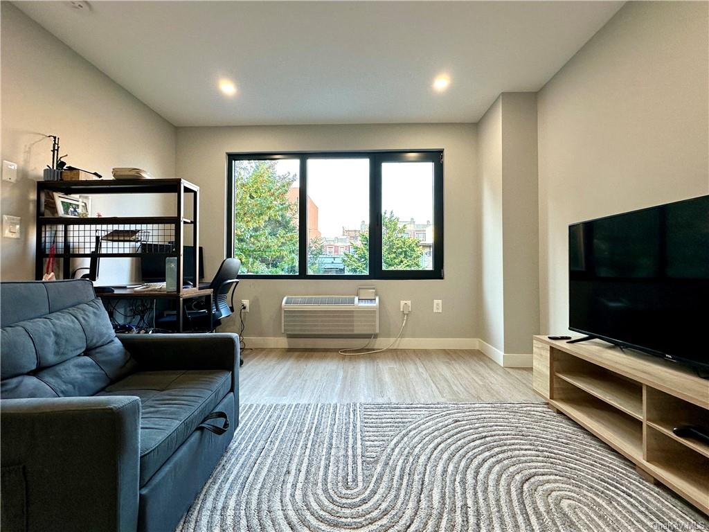 Living room with a wall mounted AC and light wood-type flooring